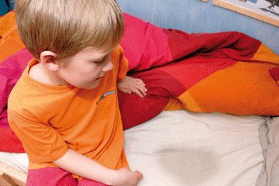 child in orange shirt sitting on wet bed